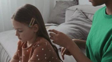 Küçük kızların saçlarını parmaklarıyla tarayan Afrikalı Amerikalı ergen bebek bakıcısının belden aşağı vuruşları rahat bir ev ortamında bir arada kalırken.