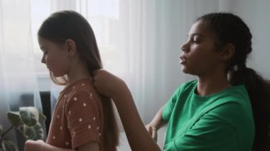 Kafkasyalı küçük bir kızın arkasında oturan ve uzun saçlarını şefkatle tarayan Afrikalı Amerikalı bir bebek bakıcısının göğüs kafesi.