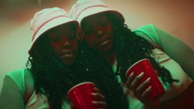 Kova şapkalı ve üstünde duvar aynasına yaslanmış, tek kullanımlık alkolle fotoğraf makinesine bakan örgü kollu güzel Afro-Amerikan bir bayanın göğsünden portresi.