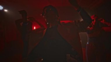 Elektronik müzik eşliğinde dans eden ve gece kulüpte kırmızı neon ışıkları ve tekrarlanan yanıp sönen ışıklarla eğlenen bir grup genç enerjik partiden oluşan el kameraları.