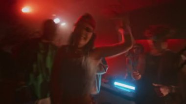Gece kulübünde, kırmızı neon ışıkları ve tekrarlanan yanıp sönen ışıklarla dans eden 2K kıyafetli, modaya uygun bir bayanın bulanık el kamerası görüntüsü.