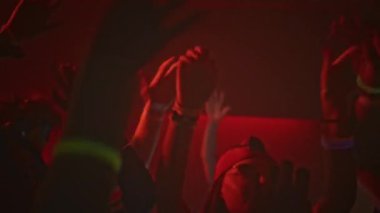 Elektronik müzik eşliğinde dans ederken el ele tutuşan ve gece boyunca yanıp sönen kırmızı ışıklı kulüpte eğlenen genç partilerin yüksek kesiminden bir sahne.