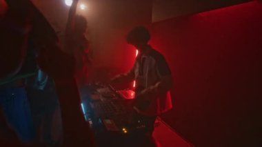 Eşofmanlı havalı DJ 'in Red Neon Light Gece Kulübü' ndeki parti sırasında çılgın kalabalığa müzik eşliğinde elektronik dans müziği çalması.