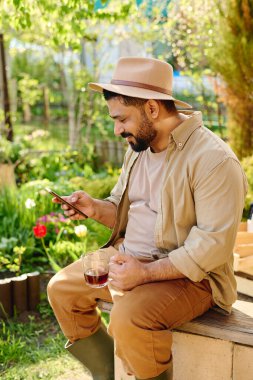 Mutlu sakallı erkek çiftçi cep telefonuyla online video mu izliyor yoksa bahçede otururken görüntülü sohbet mi ediyor?