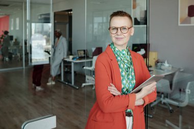 Tablet tutan kendine güvenen iş kadınının portresi cam duvarlı ofis ortamında arka planda meslektaşlarıyla dikilirken