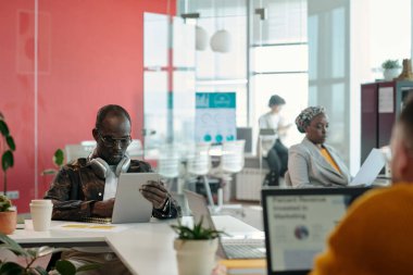 Ofis toplantısına katılan, raporları inceleyen ve ortak çalışma ortamında fikirleri paylaşan profesyoneller