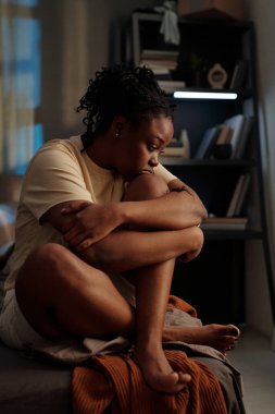 Geceleri uykusuzluk çekerken pijamalı, dizlerine ve çenelerine dokunan kasvetli Afrikalı Amerikalı kadın.