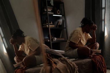 Yatağa oturmuş sevgilisinin fotoğraflarına bakan, tişörtlü ve şortlu Afro-Amerikan genç bir kadının yan görüntüsü.