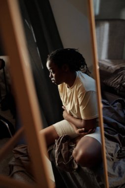 Yatakta oturan çaresiz genç kadının yansıması ve travma sonrası sendromun neden olduğu düşünceler üzerine yoğunlaşıyor.