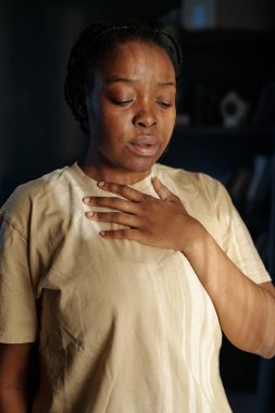 Tişörtlü genç bir kadın elini göğsünde tutuyor. Travma sonrası sendrom belirtileriyle uğraşırken nefes alıyor ve nefes veriyor.