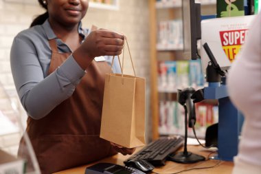 Kozmetik süpermarketinin genç bayan tezgâhtarının, dükkandaki tezgahın üzerinden tüketiciye sattığı kağıt torbaları kestiği sahneler.