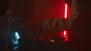 Kırmızı neon gece kulübündeki retro partisinde genç kıvırcık saçlı adamın elektronik dans müziği çalıp DJ karıştırma masasını kullanarak sürekli yanıp sönen flaşlarla değiştirmesi.