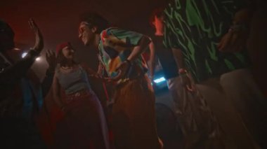 Gece kulübündeki retro partisinde parlak elbiseli, parlak elbiseli, genç çılgın gençlerin dans ettiği, kırmızı neon ışıklı ve sürekli yanıp sönen pozitif hipster 'ın yavaşlığını yakınlaştır ve uzaklaştır.