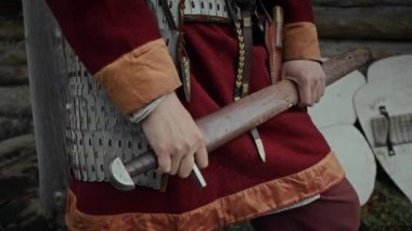 Orta ölçekli yakın çekim elleri ve kırmızı ceketli tanınmayan Orta Çağ askerinin orta kesimi, tarihi kalede korumacı metal zırh, ahşap bir kılıç taşıyor.