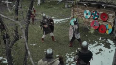 Orta Çağ garnizonundaki zırhlı askerlerin, ortaçağ kasabasını korurken kılıç talimi yaparken, rakibini tekmelerken, yere yığılırken ve yoldaşları izlerken yüksek açılı çekimleri.