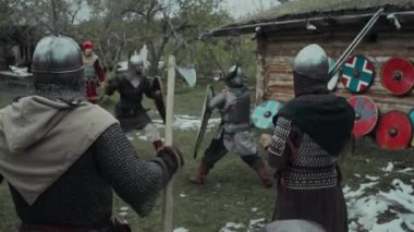 İki ortaçağ savaşçısının zırhlı göğüs zırhları ve miğferleri kuşanmış savaş için eğitim alırken balta ve kalkanları ellerinde tutarken yoldaşlar izleyip, tezahürat yapıp, savaş baltalarını sallarken.