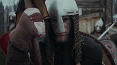 Zincirli miğfer takmış, mızrağa dayanmış, silahlı arkadaşlarıyla kale kapısının önünde poz verirken kameraya bakan yorgun, yorgun, beyaz erkek gardiyanın portresi.