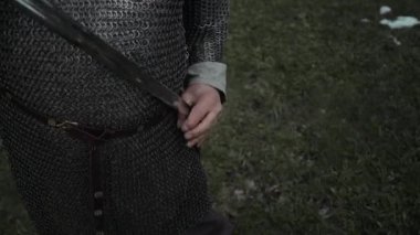 Zincirli tunik ve keten gömlekli tanınmayan bir erkek savaşçının orta boy orta kesim fotoğrafı. Açık havada dururken kılıcını kınına geri sokmuş.