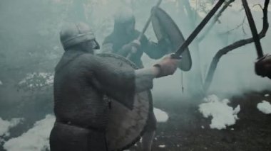 Miğferli ve zırhlı iki Orta Çağ askerinin, şövalyelerle savaşırken, iki kılıç kullanırken, kalkanlarla savaşırken, feodal şatoda kalkanları yanarken orta büyüklükte bir fotoğrafı.