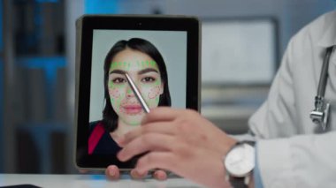 Stylus ve tablet tutan isimsiz kozmetik uzmanının eline bıçak darbesi. Yüzünde çizgiler olan kadının fotoğrafı. Modern klinikte yüz hatlarını düzeltmenin ve şekillendirmenin yollarını anlatıyor.