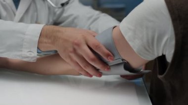 Klinikte yıllık kontroller sırasında kan basıncını tonometreyle ölçmek için laboratuvar önlüklü, isimsiz hastaların kollarına kelepçe takan tanınmayan doktorların yan çekilmiş fotoğrafları.