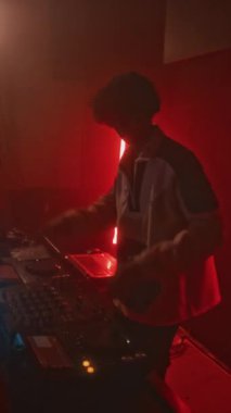 Kırmızı neon ışıklı gece kulübünde çılgın kalabalığa karşı eşofmanlı havalı DJ 'in elektronik dans müziği eşliğinde dikey çekimleri.