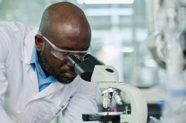 Koruyucu gözlüklü genç bilim adamı mikroskoba bakarken yeni bir tür veya zehirli kimyasal madde üzerinde çalışıyor.