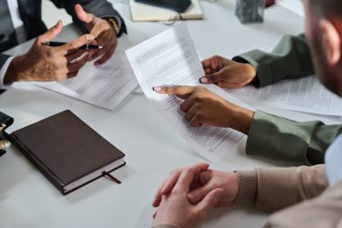 Gri formalı genç, tanınmayan kadın hukukçu ofisteki müşteriye bilgi verirken sözleşme metnini işaret ediyor.