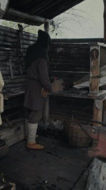 Ortaçağ demir ocağında çalışan erkek demircinin tam dikey çekimi körük kullanarak kömürleri ısıtmak, ocakta metal ısıtırken havaya hava üflemek.