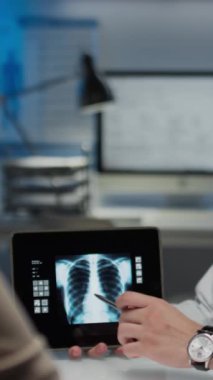 Anonim pulmonoloğun hastaya kablosuz tablette akciğer röntgeni görüntüsü gösterirken dikey görüntüsü ve modern klinikte teşhis koyuyor.