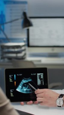 Ultrason ya da ultrason görüntüleriyle elinde tablet bulunan tanınamayan sonolojistin dikey görüntüsü ve özel klinikteki tanımlanamayan hastaya sonuçları açıklarken.