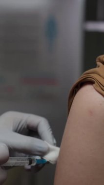 Korumalı eldivenler giymiş, kimliği belirsiz doktorların ellerinin dikey kapanması, enjeksiyon bölgesini alkol ile sterilize etmesi ve modern hastanedeki hastaların omuzlarına aşı yapılması.