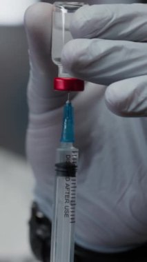 Bulanık immünologların dikey yakın çekimi koruyucu eldivenler veriyor. Klinikte aşı yapmadan önce havayı temizlemek için ilaç ve şırıngayı şişeden çekiyorlar.