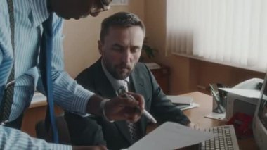 Beyaz sakallı deneyimli bir ofis çalışanının çeşitli meslektaşlarına dokümanlarla ilgili tavsiyeler verirken ve 90 'ların retro ofisinde modası geçmiş bilgisayar üzerinde çalışmaya devam ederken orta boy fotoğrafı.