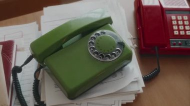 Kimse yeşil zeytin renginde, yuvarlak telefonu ahşap masadaki dokümanların üzerinde 90 'ların ofis telefonunun yanındaki parlak kırmızı sabit telefonun yanında göremez.