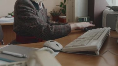 Kareli ceketli ve kare gözlüklü güzel sarışın beyaz bir çalışanın disket seçerken ve 90 'lı yıllarda ofiste çalışırken eski bir bilgisayara takarken yan yatmış görüntüleri.