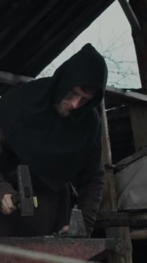 Ortaçağ demirciliğinde çivi ya da ev aletleri döverken metal üzerine çekiçle vurulan odaklanmış beyaz demircinin orta dikey görüntüsü.
