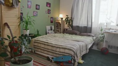 Genç bir çocuğun ya da genç bir erkek öğrencinin yatak, gardırop, gitar, kaykay, bilgisayarlı masa, ekranda duraklatılmış video oyunu...