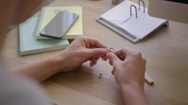 Sıradan temizlikten sonra kolej defterleri ve akıllı telefonuyla protez koklear kulak implantı parçaları birleştiren tanınmayan genç bir erkek öğrencinin omuz üstü fotoğrafı.