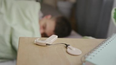Evdeki masada yatan elektronik koklear implantın yakın plantı, genç sağır bir adamın eli sabah uyanır ve onu alır.