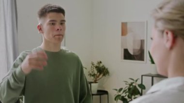 İşitme cihazı olan 16 yaşındaki beyaz bir çocuğun, kadın öğretmeniyle birlikte, işaret dilinde nasıl olduğunu sorarken, ASL öğrenirken orta omuz üstü fotoğrafı.