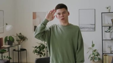 İşitme engelli, beyaz, sağır ve dilsiz bir adamın orta boy portresi. Amerikan işaret dilinde el hareketleriyle kameraya bakıp gülümsüyor musunuz diye soruyor.