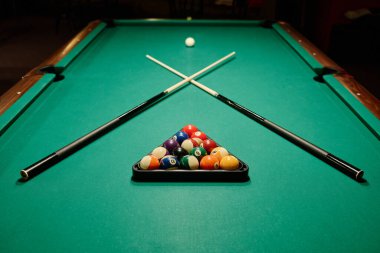 Uzun ve geniş bilardo masasının bir parçası. Üzerinde iki çapraz işaret var. Beyaz top ve farklı renkte toplar arasında yatıyorlar.