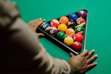 Yeşil bilardo masasının önünde duran ve toplarla üçgen askıya dokunan tanınmayan genç adamın yüksek açılı elleri.