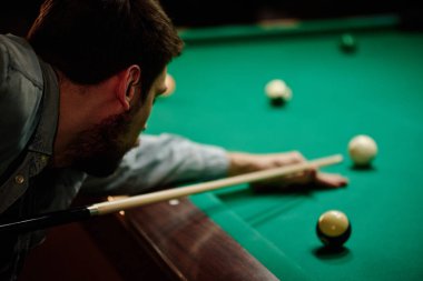 Genç erkek bilardo oyuncularına odaklanın. Yeşil masaya eğilip oyun odasında oynarken, günlük kıyafetleri giyin.