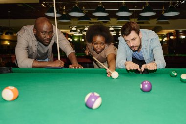 Afro-Amerikan bir kızın yanında duran ve ona bilardo oynamayı ve top oynamayı öğreten genç bir adam.