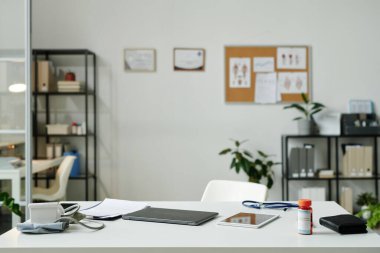 Katlanmış dizüstü bilgisayarı, tableti, tonometresi ve ilaç şişesi olan dijital sağlık çalışanlarının çalıştığı modern geniş sağlık merkezinin bir parçası.