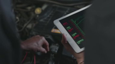 Tanımlanamayan erkek ve kadın tamircilerin, tablet bilgisayarlarını araç tanılama programı ile tutarken, araba motorlarını kontrol ederken ve performans verilerini tartışırken, yakın çekimde omuz üstü çekimleri.