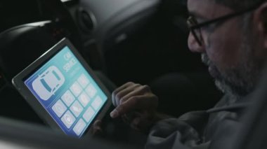Karmaşık kontrol sırasında müşteri arabasında oturan, elektrik ve işletim sistemlerini test eden, otomobil servis yazılımlı tablet bilgisayarlara bakan orta yaşlı Asyalı araba tamircisinin yakın çekimi