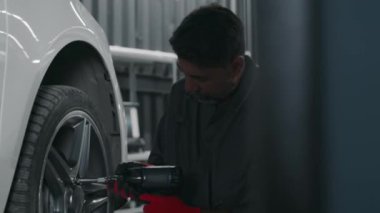 Yetişkin Hintli tamircinin gri tulumlu orta boy fotoğrafı, atölyedeki arızalı lastiği tamir ettikten sonra müşteri arabasının tekerleklerini sıkan kırmızı eldivenler.
